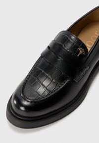 Schwarze Lederloafers mit einem Krokodilmuster, ausgestattet mit einem doppelten Riemen und einem kleinen goldenen Emblem an der Seite. Glatte Textur und abgerundete Zehenpartie.