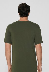 Oliwkowa koszulka z krótkim rękawem, wykonana z gładkiej bawełny, z klasycznym okrągłym dekoltem i luźnym krojem, widziana od tyłu.