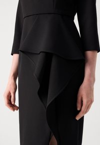Abito nero con design a peplum, caratterizzato da un orlo arricciato e testurizzato e maniche a tre quarti, che mette in evidenza un tessuto liscio e linee pulite.