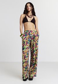 Pantalons amples à motifs avec un design coloré en vert, bleu, rose et jaune sur un fond clair. Fabriqués en tissu léger avec des poches.