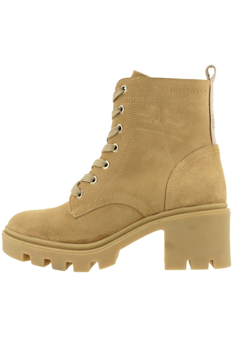 Botas de tobillo de ante color arena con suela gruesa y texturizada, con cordones en la parte delantera y talón reforzado. Logotipo grabado en el lateral.