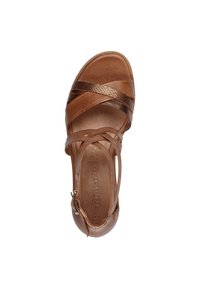 Brown leather sandal featuring cross straps, a rounded toe, and a low heel. Textured bronze accents enhance the design. Adjustable ankle strap.