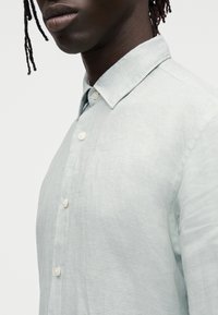 Hellgrünes Hemd aus strukturiertem Stoff mit klassischem Kragen und Perlmuttknöpfen vorne und an den Manschetten.