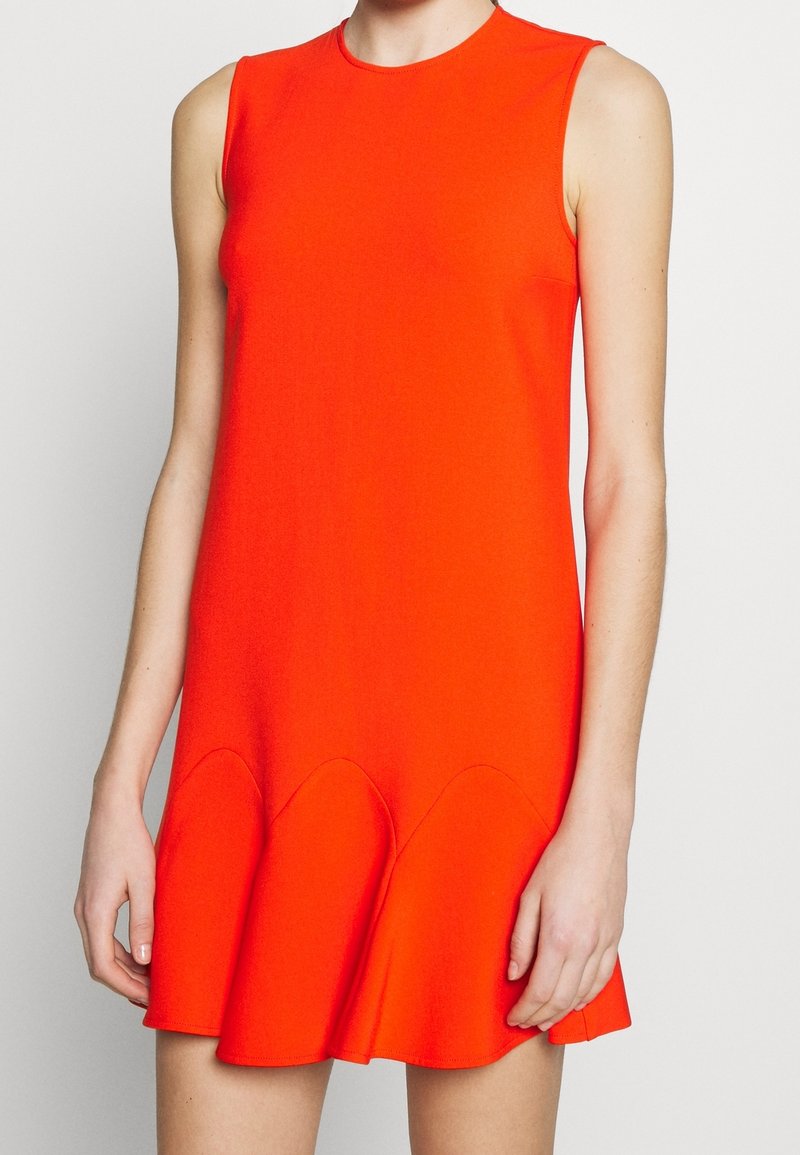 Červené šaty bez rukávů s přiléhavým korzetem, rozšířeným lemem a vroubkovanými detaily na spodní části, vyrobené z hladkého, elastického materiálu.