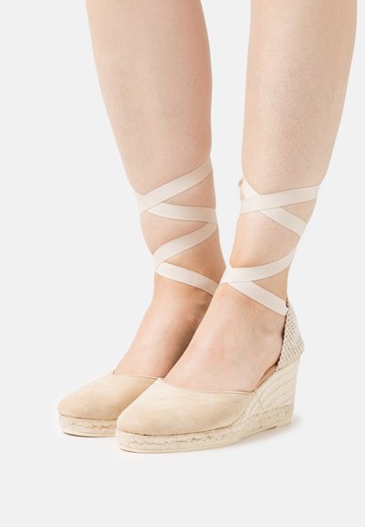 Espadrillas con zeppa in suede beige, caratterizzate da un tacco testurizzato, lacci alla caviglia in tessuto beige intrecciati e una piattaforma in juta intrecciata.