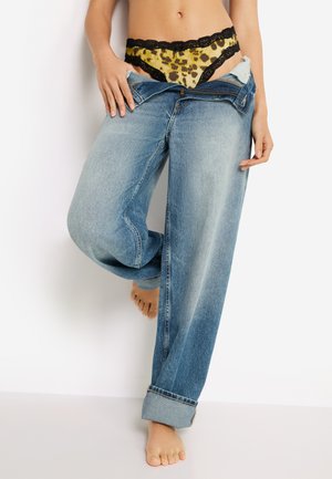 Vaaleanpesetyt rentomalliset farkut, joissa on käännettävät resorit; alla keltainen leopardikuvioinen pitsitanga mustilla reunoilla.