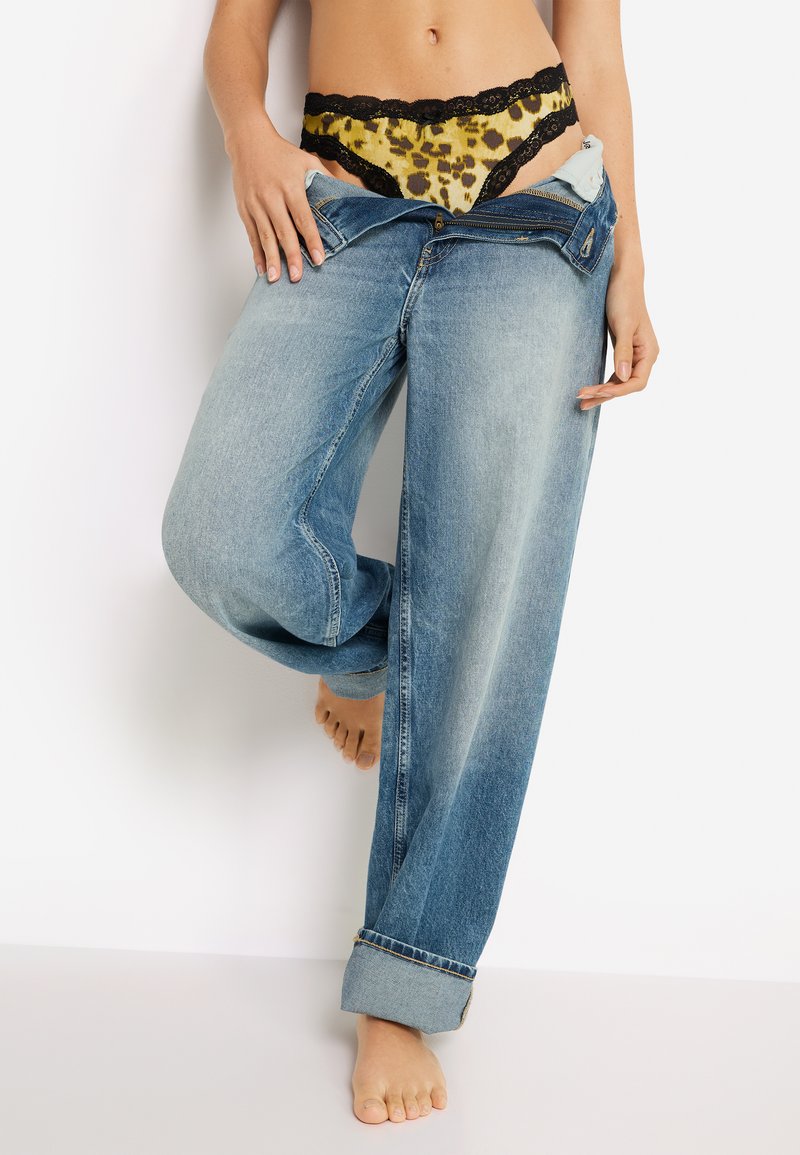 Τζιν παντελόνι με ανοιχτό ξέπλυμα, άνετη εφαρμογή, με γυρισμένα μανίκια· από κάτω ένα κίτρινο  στρινγκ από δαντέλα με λεοπάρ σχέδιο και μαύρο περίγραμμα.