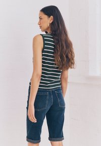 Maiou fără mâneci cu dungi verzi și albe, asortat cu pantaloni scurți din denim albastru închis cu tiv răsucit, văzut din spate.