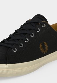 Μαύρο πάνινο Sneaker με μαύρα κορδόνια, ασημένια ρούμπτσα, μπεζ σόλα και καφέ κεντητό λογότυπο με στεφάνι δάφνης στο πλάι.