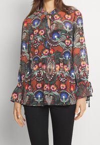 Hnědá květinová blůza s nafouknutými rukávy, výstřihem ve tvaru klíče a nařaseným pasem. Obsahuje barevné vzory květin a listů v modré, červené a zelené barvě.