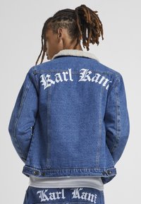 Jeans jakna v modri barvi s krznjenim ovratnikom, na zadnji strani z belim napisom "Karl Kani". Klasična zasnova, ravna krojna in gumbi.