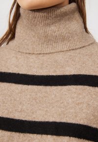 Pull à col roulé en mélange de laine beige avec des rayures horizontales noires. Texture côtelée au niveau du col, le corps présente une finition douce et bross ée.
