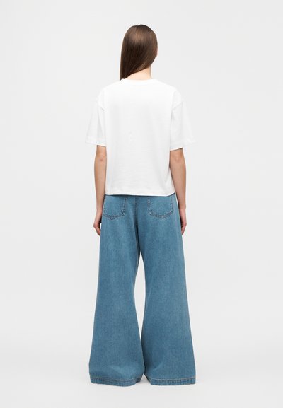 Λευκό βαμβακερό t-shirt με κομμένη γραμμή, συνδυασμένο με φαρδιά, ανοιχτού μπλε τζιν παντελόνια με ξεθωριασμένο πλύσιμο και πίσω τσέπες.
