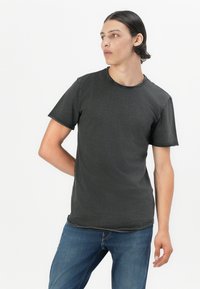 Dunkelgraues T-Shirt mit kurzen Ärmeln und Rundhalsausschnitt sowie kontrastierendem Stich, kombiniert mit blauen Jeans. Glattes Material, normale Passform.