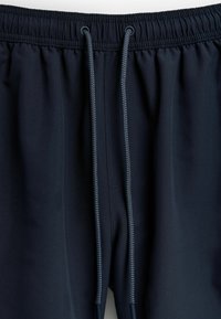 Pantaloni jogger bleumarin cu talie elastică, cordon de ajustare și textură netedă; prezintă cusături fine și o croială relaxată.