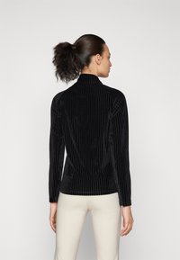 Schwarzes, geripptes Samt-Hemd mit langen Ärmeln und hohem Kragen, slim fit geschnitten und mit strukturierter Oberfläche, kombiniert mit hellen Hosen.