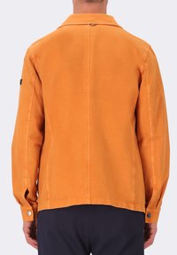 Giacca in cotone arancione con colletto, maniche lunghe e bottoni a pressione. Presenta una texture liscia e dettagli minimali.
