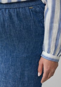 Donkerblauwe denim rok met een geplooide taille en subtiele textuur. Een witte en blauwe gestreepte mouw is gedeeltelijk zichtbaar ernaast.