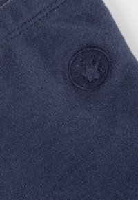 Tessuto di cotone blu navy con una texture sottile, caratterizzato da un logo circolare in rilievo nella parte superiore sinistra. Design semplice e lineare.