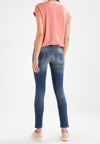 Ljusrosa t-shirt med uppvikt ärm, kombinerad med blå skinny jeans. Jeansen har bakfickor och en blekt tvätt. Lätta skor fulländar outfiten.