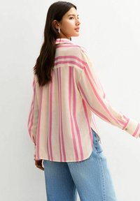 Camisa de botones a rayas en una tela suave, con rayas horizontales en rosa y crema, mangas largas y un dobladillo redondeado. Se muestra la vista trasera.