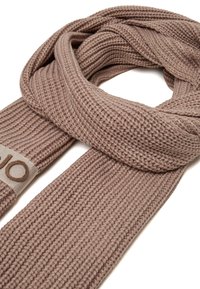 Sciarpa lavorata a maglia in un morbido colore beige, con una texture a coste e un'etichetta in tessuto semplice con lettering ricamato.