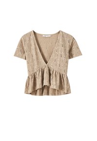 Beige kortærmet bluse med en tekstureret honningcomb-mønster, en dyb V-hals og en peplum-søm. Let materiale og afslappet pasform.