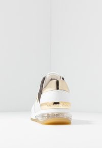 Sneaker bianco e grigio con tallone in metallo dorato e suola trasparente, con texture perforate e lisce. Nome del marchio visibile sul tallone.