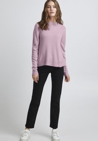 Rosa, strukturerad stickad tröja med långa ärmar, rund halsringning och ribbad nederkant, i kombination med svarta slim-fit byxor och vita sneakers.