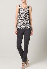Czarna i biała bezrękawnik z luźnym krojem, kwiatowym wzorem i dekoltem w kształcie łezki, zestawiony z dopasowanymi ciemnymi spodniami i beżowymi szpilkami.