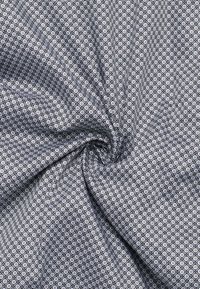 Grau gemustertes Gewebe mit kleinen weißen Quadraten, das über eine strukturierte Webart verfügt. Das Material wirkt weich und fällt geschmeidig.
