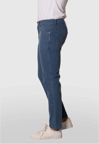 Jeans de mezclilla azul con corte ajustado, que cuentan con cinco bolsillos, herrajes de metal y un sutil detalle de costura. Combinados con zapatillas blancas.