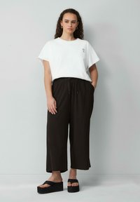 Witte korte mouwen t-shirt met bloemenborduursel, gecombineerd met zwarte losvallende broek en dikke zwarte platform sandalen.