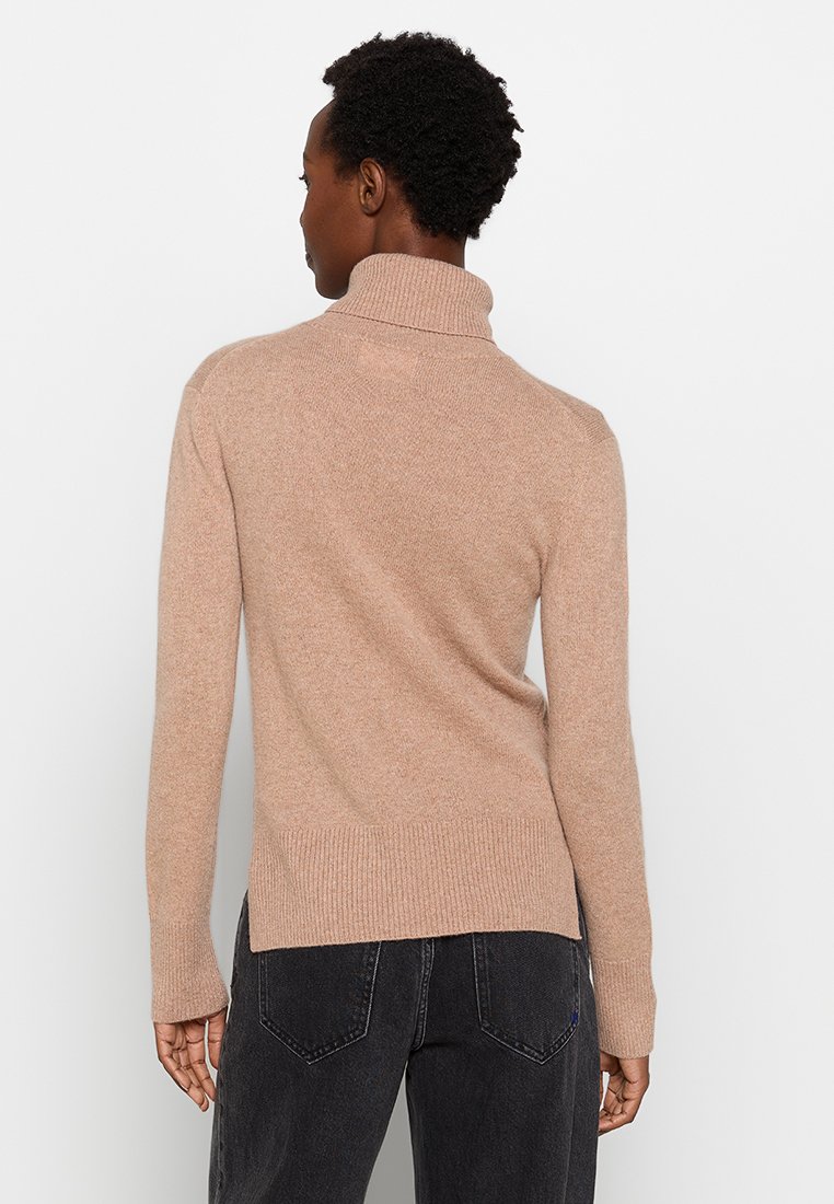 Beżowy sweter z golfem o teksturowanym wykończeniu, z prążkowanym dołem i bocznymi rozporkami, wykonany z miękkiego materiału. Pokazany z tyłu.