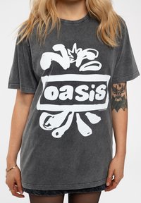 Gray oversized t-shirt made of cotton, featuring a large white graphic logo with the word "oasis" and abstract designs. Short sleeves, relaxed fit.