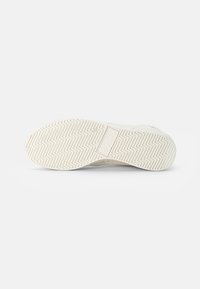 White sneaker bottom with herringbone tread pattern, embossed logo, and a textured finish. Rubber material with a smooth, flexible design.