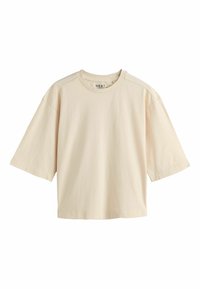 T-shirt en coton beige oversized à manches courtes avec encolure ronde et ourlet droit, étiqueté "NEXT" à l'intérieur du col.