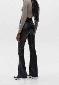 Pantalon évasé en similicuir noir avec une taille haute, une texture lisse et des poches arrière. Associé à un haut court olive moulant.