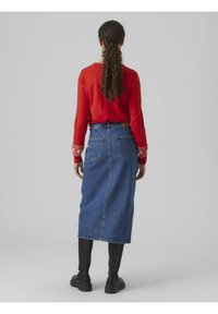 Rode top met lange mouwen en gemusterde manchetten, gecombineerd met een blauwe denim midi-rok. De outfit heeft een rechte silhouette en functionele achterzakken.