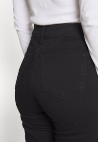 Högmidjade svarta jeans i denim, med en ficka bak, slät yta och en figurnära design.