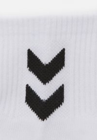 Calcetines blancos con patrón de chevron negro; la textura del tejido es de punto, con un puño acanalado y un diseño geométrico en contraste.