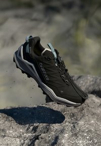 Melnas sporta kurpes ar sintētisku augšdaļu un pelēkiem akcentiem, piedāvājot auklu slēgšanu, teksturētu zoli un vieglu konstrukciju.