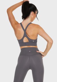 Il reggiseno sportivo grigio presenta un design incrociato sulla schiena con un'apertura a forma di chiave. I leggings a vita alta abbinati completano l'outfit sportivo.