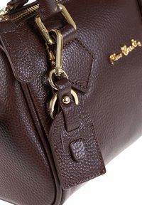 Borsa a mano in pelle marrone con superficie granulosa, dotata di hardware dorato, etichetta rimovibile e superficie testurizzata. Chiusura a zip e forma strutturata.