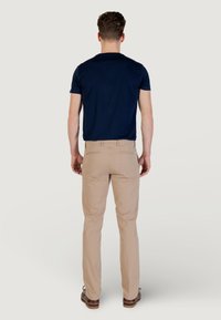 Camiseta de manga corta azul marino combinada con chinos de color beige claro. Corte suelto, textura suave, con los bolsillos traseros visibles en los pantalones. Zapatos marrones.