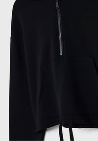Felpa nera corta realizzata in materiale morbido, con zip frontale e tasca anteriore, strings regolabili sull'orlo e texture liscia.