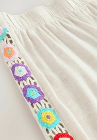 Indumento color crema con vita elastica, caratterizzato da un bordo in pizzo adornato con esagoni all'uncinetto multicolori in arancione, viola e blu.
