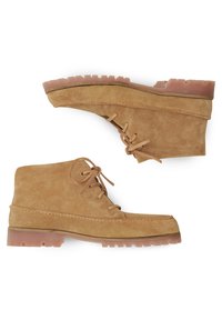 Botines de ante en tono arena con punta redondeada, diseño de cordones y suela de goma gruesa con tacos pronunciados para mayor tracción.