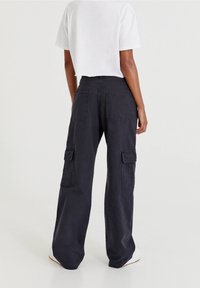 Mustat cargo-housut, joissa on löysä istuvuus, sivutaskut ja takataskut. Kangas näyttää kestävältä ja siinä on matta pinta.