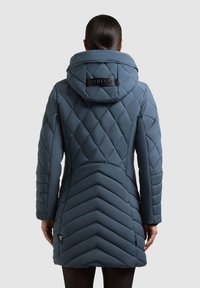 Padded modrá zimná bunda s prešívanými diamantom a chevronovými vzormi, nadmerná kapucňa a logo detail na chrbte. Obsahuje dlhé rukávy.